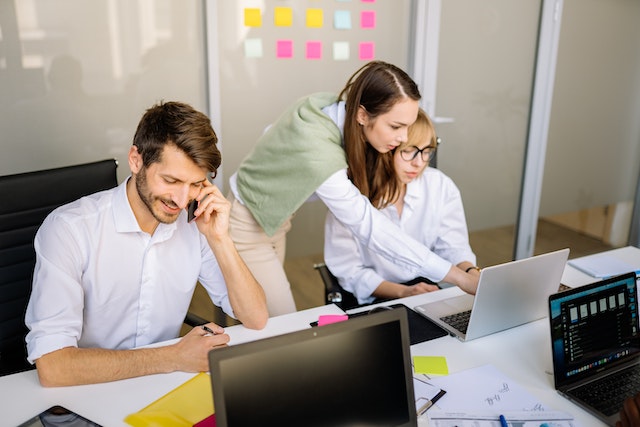 person sitting at their desk on the phone while people next to them look at something on a laptop